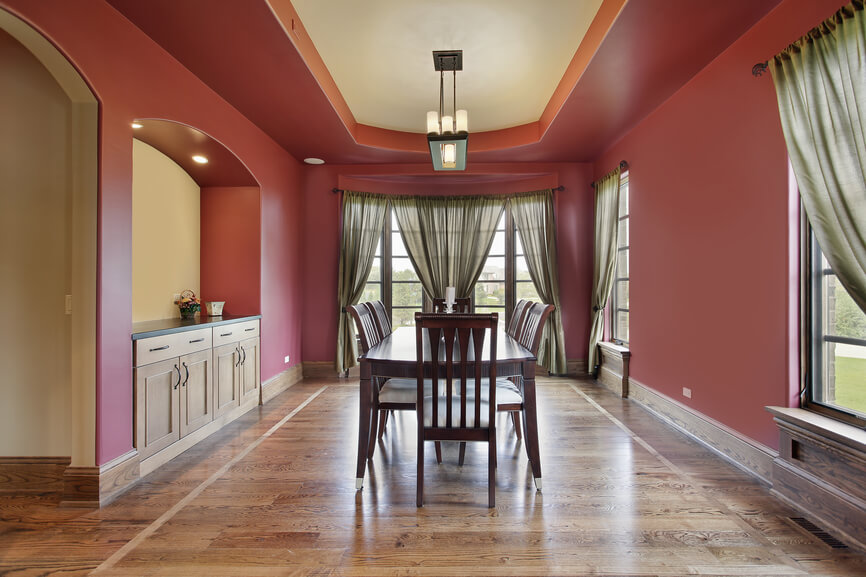 Dining room with red walls, tray ceiling and wood flooring with built-in cabinets within an alcove on one side of the room. Dining room with red walls, tray ceiling and wood flooring with built-in cabinets within an alcove on one side of the room.