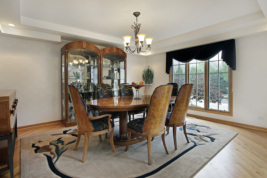 Large square dining room with oval dining table that seats seix people, custom wood dining chairs on a rug that's placed on light wood floors. Large square dining room with oval dining table that seats seix people, custom wood dining chairs on a rug that's placed on light wood floors.