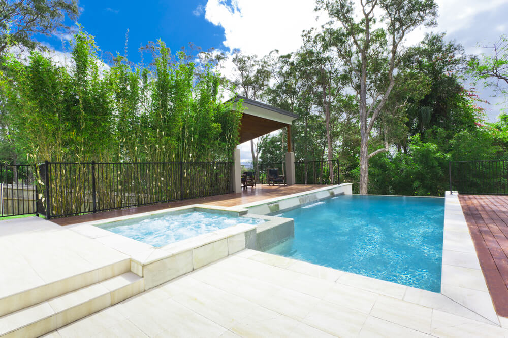 Cascading infinity pool on edge of forest with elevated hot tub. Gazebo on one side and brick patio on the other side. Cascading infinity pool on edge of forest with elevated hot tub. Gazebo on one side and brick patio on the other side.