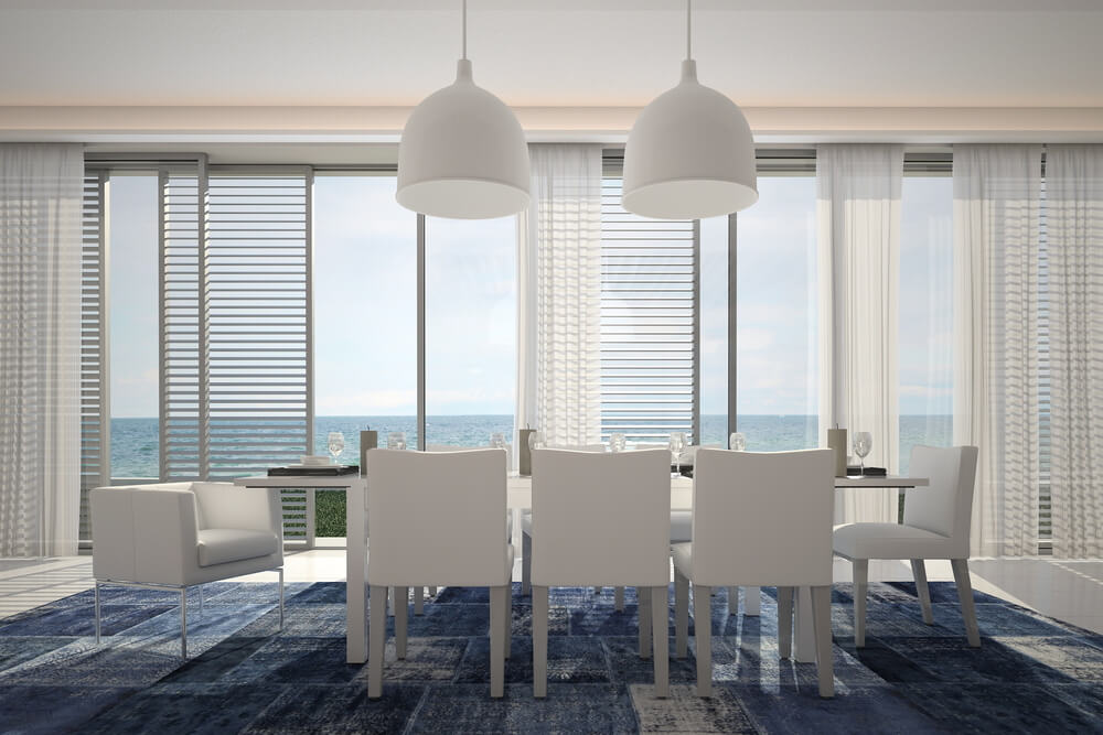 Waterfront home with dining room looking out on the ocean through full wall of floor-to-ceiling windows Waterfront home with dining room looking out on the ocean through full wall of floor-to-ceiling windows