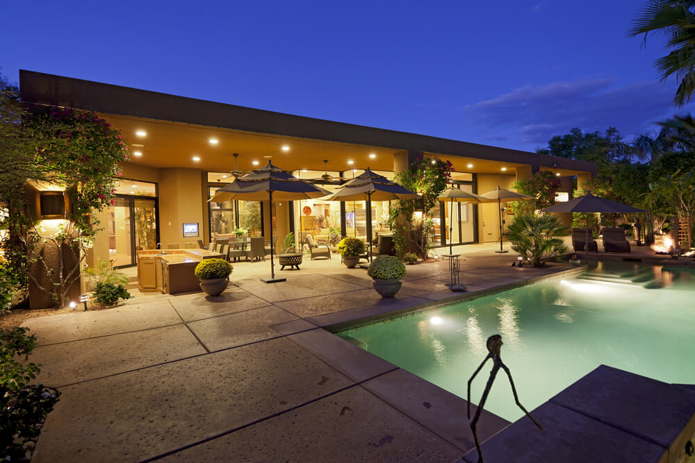 Brightly lit home and pool with large outdoor patio. Extensive trees and plants dot the patio and surround the pool. Brightly lit home and pool with large outdoor patio. Extensive trees and plants dot the patio and surround the pool.
