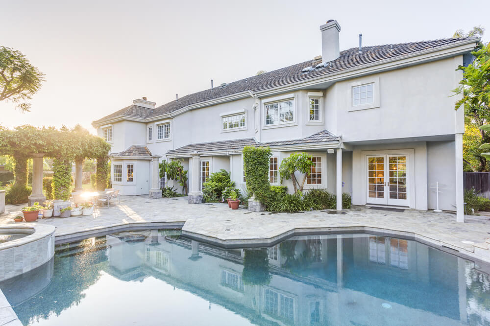 Luxury home with grey flagstone patio surrounding uniquely shaped pool and elevated hot tub. Ivy-covered pavilion adjacent to the pool provides covered outdoor seating. Luxury home with grey flagstone patio surrounding uniquely shaped pool and elevated hot tub. Ivy-covered pavilion adjacent to the pool provides covered outdoor seating.