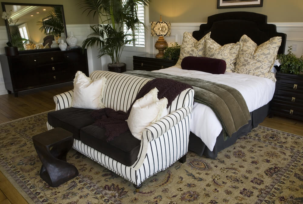 Small bedroom with impressive design details such as white wood paneling on lower half of walls, striped black and white loveseat, wood floors and dark furniture all given a breath of fresh air from potted plants. Small bedroom with impressive design details such as white wood paneling on lower half of walls, striped black and white loveseat, wood floors and dark furniture all given a breath of fresh air from potted plants.