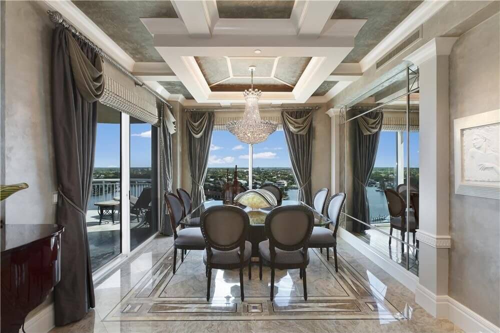 Dining room design appearing larger than it is with one wall being a floor-to-ceiling mirror and two other walls being floor-to-ceiling windows. Square glass dining table seats eight people. Dining room design appearing larger than it is with one wall being a floor-to-ceiling mirror and two other walls being floor-to-ceiling windows. Square glass dining table seats eight people.