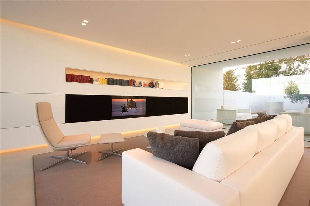 Front living room with light tan flooring and leather chair, all-white walls and black strip camouflaging television. Front living room with light tan flooring and leather chair, all-white walls and black strip camouflaging television.