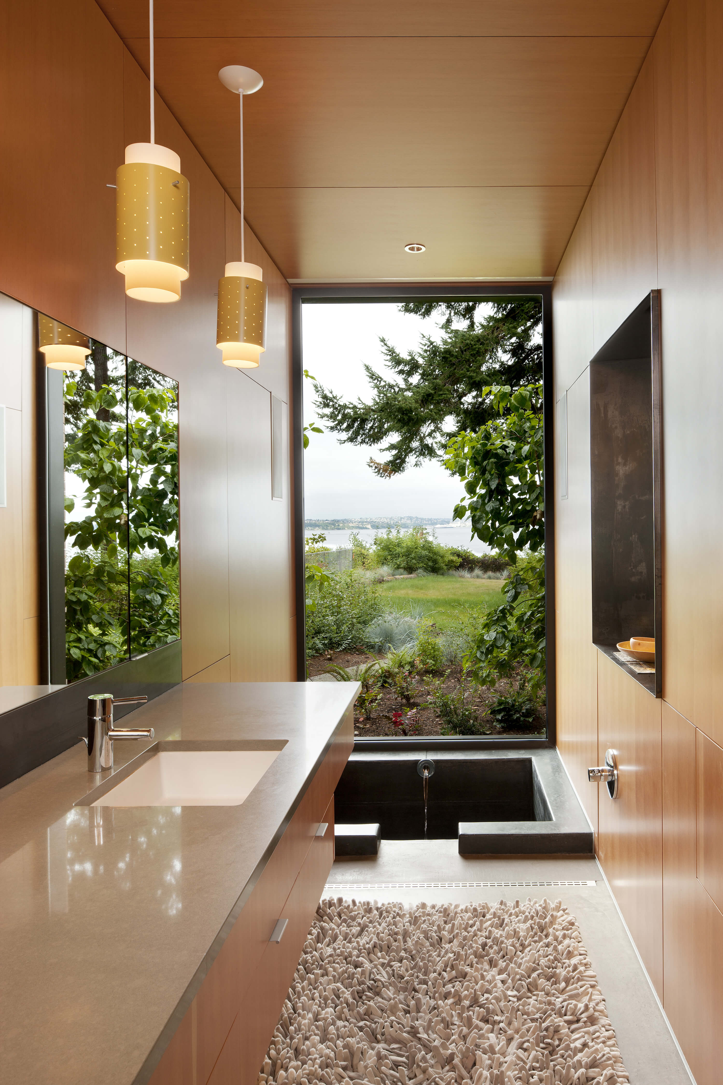 Bathroom featuring full outdoors view, sunken tub in floor and minimalist, smooth panel wood on walls and cabinetry. Bathroom featuring full outdoors view, sunken tub in floor and minimalist, smooth panel wood on walls and cabinetry.