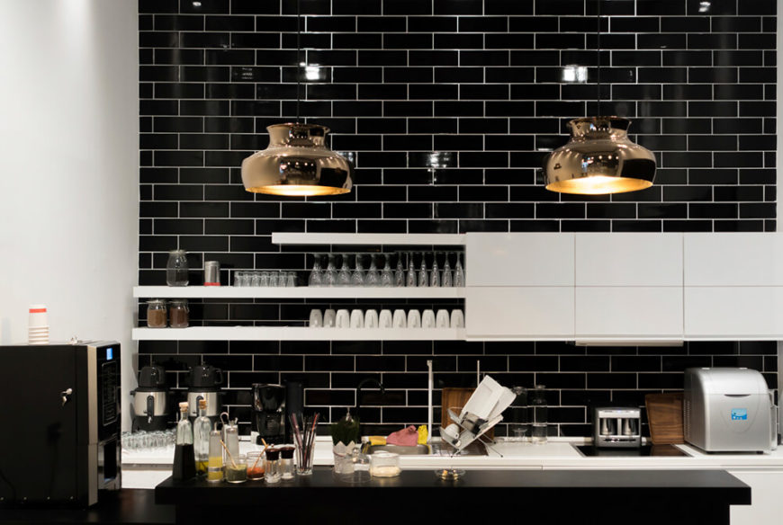 These shiny brass lights make a stunning statement against the black subway tile of this monochromatic kitchen. Golden light reflects from the insides of the pendant lights and warms up the stark kitchen colors.