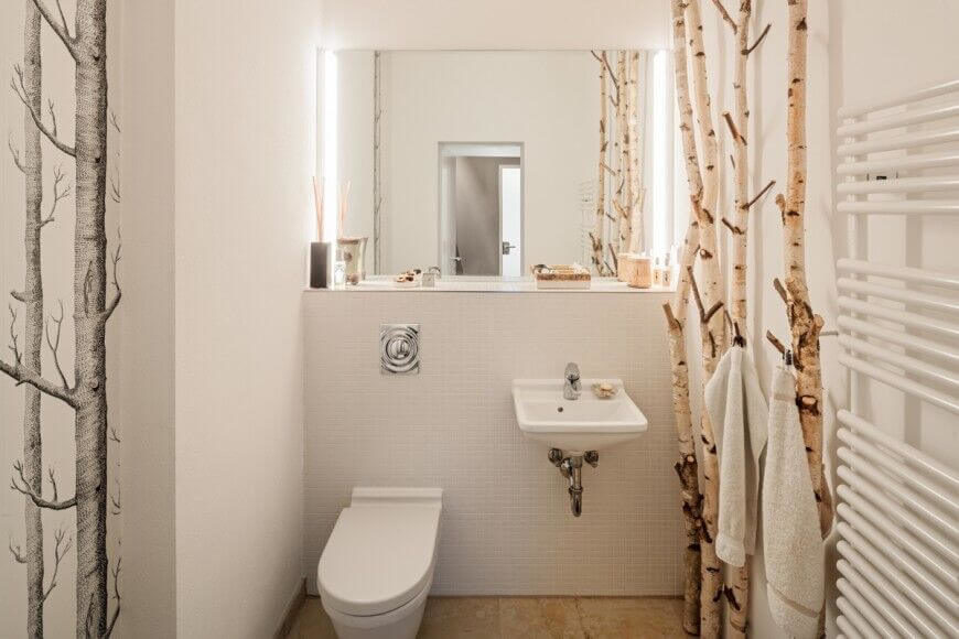 This unique space is accented by the thin birch trees standing to the side of the sink and opposite of the shower, These limbs act as both accents for the room as well as hangers for towels and clothing. Adjacent to these is a floating sink and large mirror, with a toilet directly next to the sink. This unique space is accented by the thin birch trees standing to the side of the sink and opposite of the shower, These limbs act as both accents for the room as well as hangers for towels and clothing. Adjacent to these is a floating sink and large mirror, with a toilet directly next to the sink.