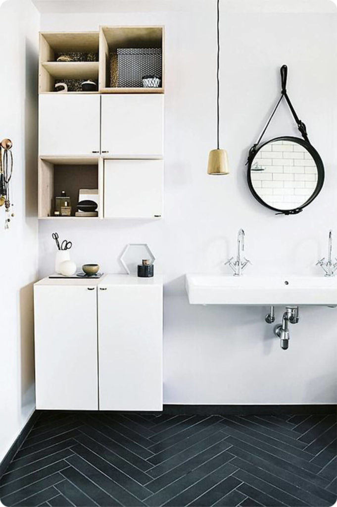 This bathroom has a stylish design with black wood paneling in a unique pattern on the floor. White walls and cabinetry contrast the dark floor, and a low hanging pendant light works with the circular mirror to add to the modern atmosphere in the room. This bathroom has a stylish design with black wood paneling in a unique pattern on the floor. White walls and cabinetry contrast the dark floor, and a low hanging pendant light works with the circular mirror to add to the modern atmosphere in the room.