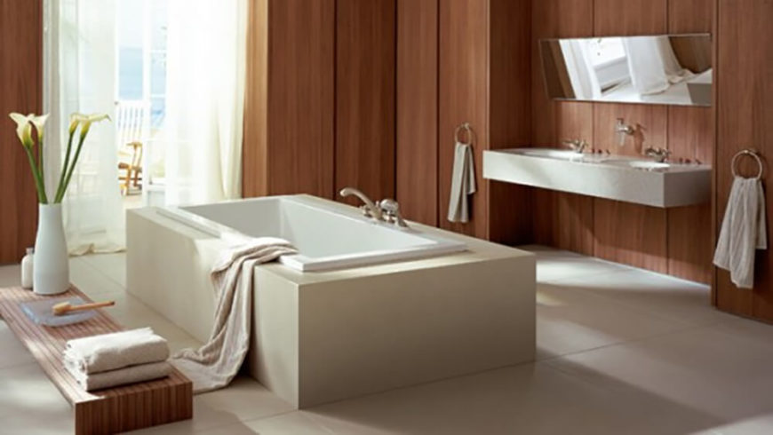 This bathroom has a very calming atmosphere, established by the rich wood panel walls and the large rectangular tub in the center of the room. A small table sits to the side of the tub and holds various toiletry items as well as decorative flowers, which also help to accent the room. This bathroom has a very calming atmosphere, established by the rich wood panel walls and the large rectangular tub in the center of the room. A small table sits to the side of the tub and holds various toiletry items as well as decorative flowers, which also help to accent the room.
