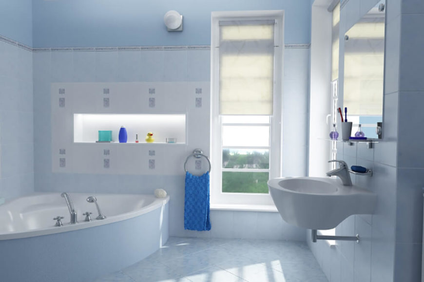 This bathroom features a light blue textured tile floor, and the tile runs up the entirety of the wall up to just below the ceiling. A floating sink hangs below a mirror with a small shelf for toiletries. There is a large corner tub, with a shelf just above the tub for storing toiletries and other decoration. This bathroom features a light blue textured tile floor, and the tile runs up the entirety of the wall up to just below the ceiling. A floating sink hangs below a mirror with a small shelf for toiletries. There is a large corner tub, with a shelf just above the tub for storing toiletries and other decoration.