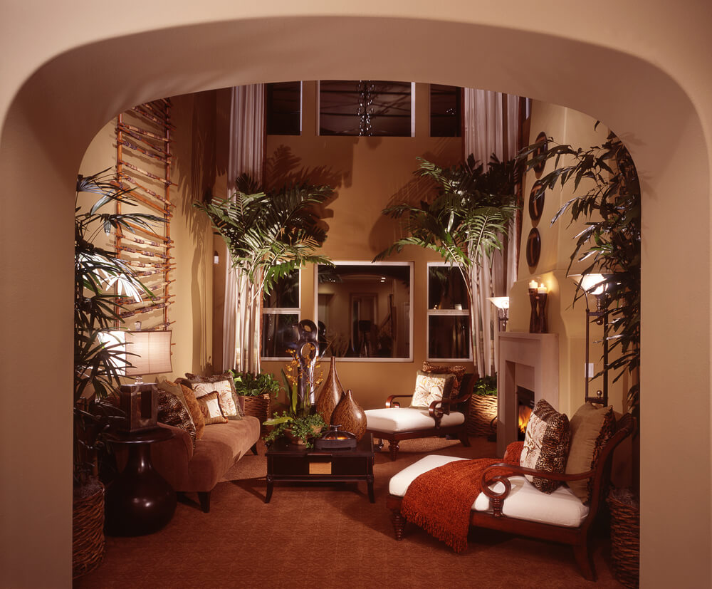 Tropical themed living room design with tall ceiling, trees, plants and formal tropical furniture accessed through an arched doorway.