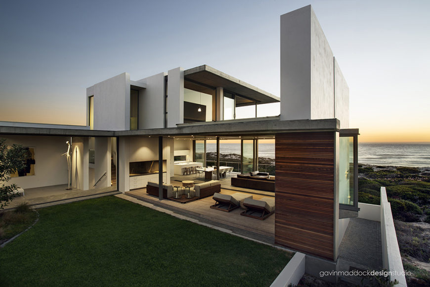 Wide view of the entire structure from oceanside, revealing the ambiguous line between indoor and outdoor spaces. Concrete slabs mix with natural wood paneling throughout the structure for unobtrusive, minimalist yet striking design. Wide view of the entire structure from oceanside, revealing the ambiguous line between indoor and outdoor spaces. Concrete slabs mix with natural wood paneling throughout the structure for unobtrusive, minimalist yet striking design.