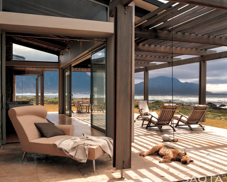 The central, open space flows directly into this sheltered seaside patio through floor to ceiling sliding glass. Set of adirondack chairs and full dining space in distance provide ample seating next to the ocean. The central, open space flows directly into this sheltered seaside patio through floor to ceiling sliding glass. Set of adirondack chairs and full dining space in distance provide ample seating next to the ocean.