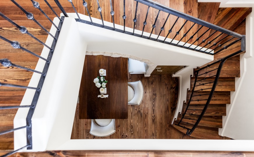 A vertical view down to the first floor reveals an expanse of rich natural wood tones on the stairs, contrasting sharply with white walls and wrought iron railing. A vertical view down to the first floor reveals an expanse of rich natural wood tones on the stairs, contrasting sharply with white walls and wrought iron railing.