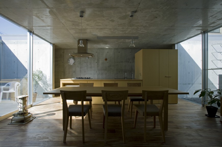 Straight on view of the kitchen and dining area. Here we see the light natural wood tones of the cabinetry and kitchen island, plus the dining set, standing out amidst the concrete grey structure. Straight on view of the kitchen and dining area. Here we see the light natural wood tones of the cabinetry and kitchen island, plus the dining set, standing out amidst the concrete grey structure.