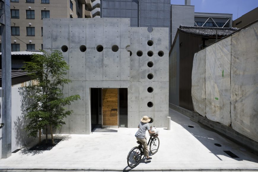 The front entrance features a natural wood door seated in a glass frame, the only detail aside the port holes lining the entire facade. The raised architecture helps separate the home from closely surrounding buildings. The front entrance features a natural wood door seated in a glass frame, the only detail aside the port holes lining the entire facade. The raised architecture helps separate the home from closely surrounding buildings.