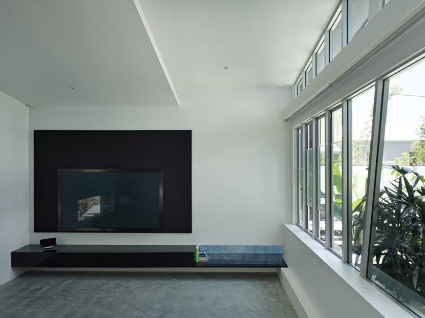 Living room with minimalist design features black media surround for the television, with singular black shelf built into the wall. Angular window frames punctuate the wall of glass at right with views of rooftop garden. Living room with minimalist design features black media surround for the television, with singular black shelf built into the wall. Angular window frames punctuate the wall of glass at right with views of rooftop garden.