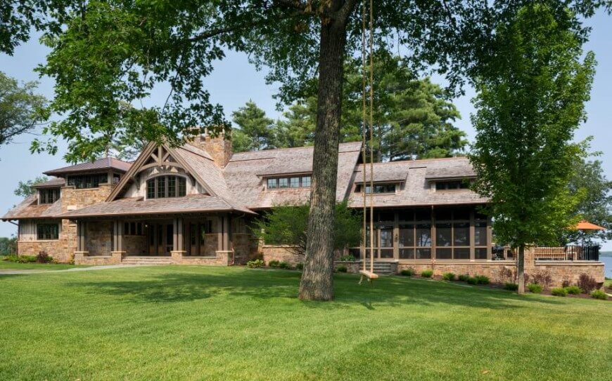 The gently sloped lawn surrounds the stone wrapped home, lowering to reveal a raised patio with wrought iron fencing at right, with multiple entrances and an array of windows scattered throughout the facade. The gently sloped lawn surrounds the stone wrapped home, lowering to reveal a raised patio with wrought iron fencing at right, with multiple entrances and an array of windows scattered throughout the facade.