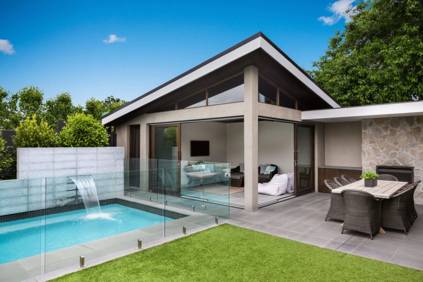 Across the back yard we see the glass wrapped pool abutting the pool house. Featuring a small living room with sliding glass panels to openly share space with the patio, the pool house also boasts a full, discrete bathroom facility. Across the back yard we see the glass wrapped pool abutting the pool house. Featuring a small living room with sliding glass panels to openly share space with the patio, the pool house also boasts a full, discrete bathroom facility.