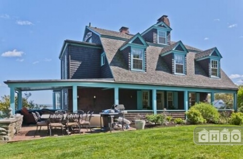 The exterior of the home has a gorgeous blue trim to brighten up the brown siding. A front patio sits near the front porch. The home sits on a large yard that includes gardens and manicured landscaping. The exterior of the home has a gorgeous blue trim to brighten up the brown siding. A front patio sits near the front porch. The home sits on a large yard that includes gardens and manicured landscaping.