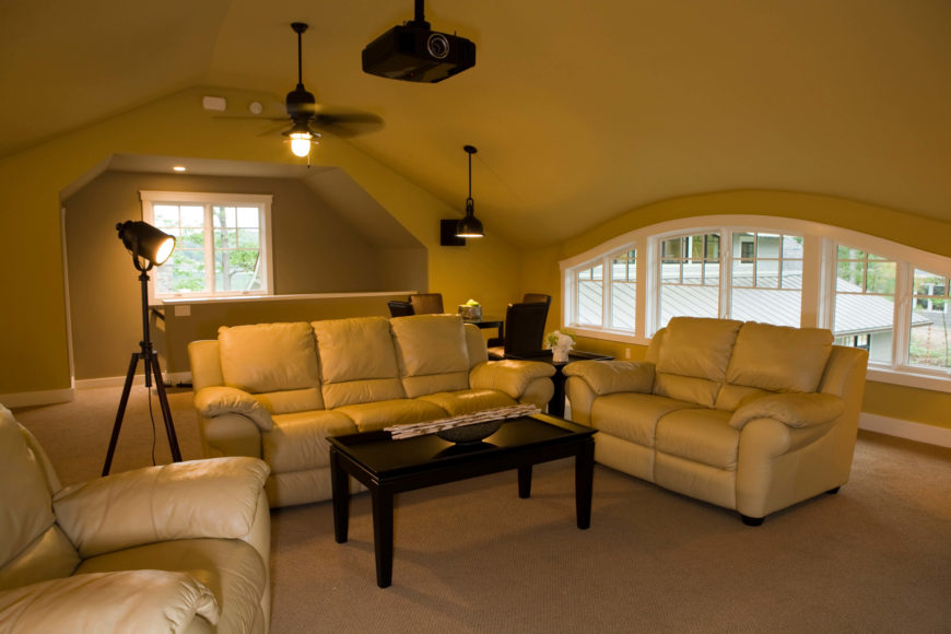 Upper level family room is a perfect space for entertaining and watching movies, with a projector hanging over a trio of plush leather seating options and jet black coffee table. A wide span of windows allows for natural light, while film-set-style floor lamp helps set the mood. Upper level family room is a perfect space for entertaining and watching movies, with a projector hanging over a trio of plush leather seating options and jet black coffee table. A wide span of windows allows for natural light, while film-set-style floor lamp helps set the mood.