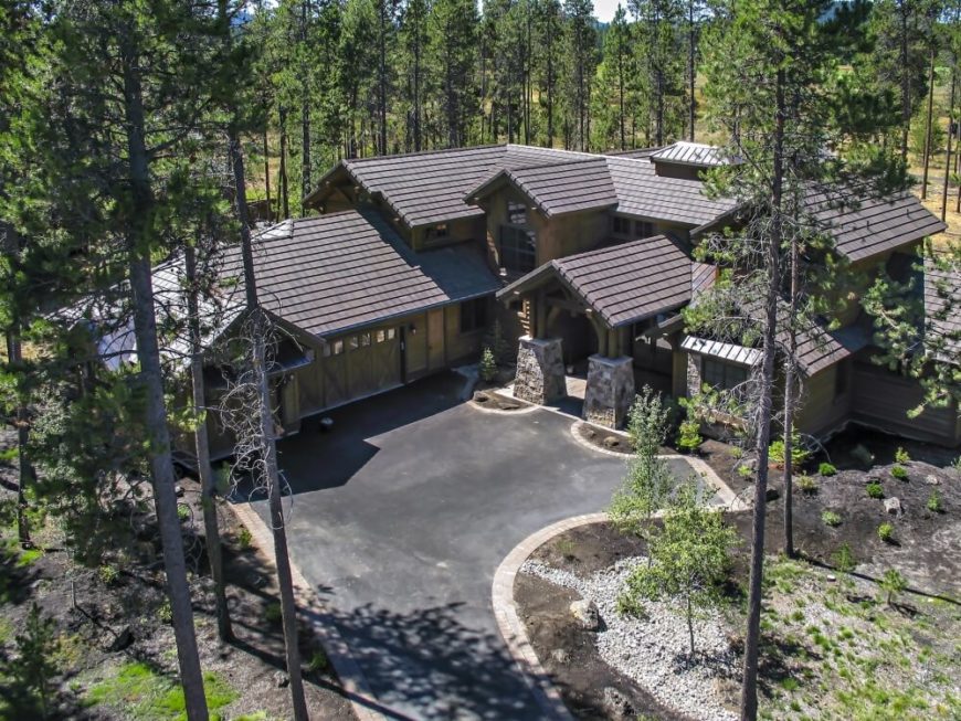 An aerial view of the home's driveway and front entrance, including the large covered entryway with stone supports and ornate woodwork. The enormous three-stall garage gives this home a L-shape. The landscaping is sparse and easy to care for, and the home is surrounded by tall pines. An aerial view of the home's driveway and front entrance, including the large covered entryway with stone supports and ornate woodwork. The enormous three-stall garage gives this home a L-shape. The landscaping is sparse and easy to care for, and the home is surrounded by tall pines.