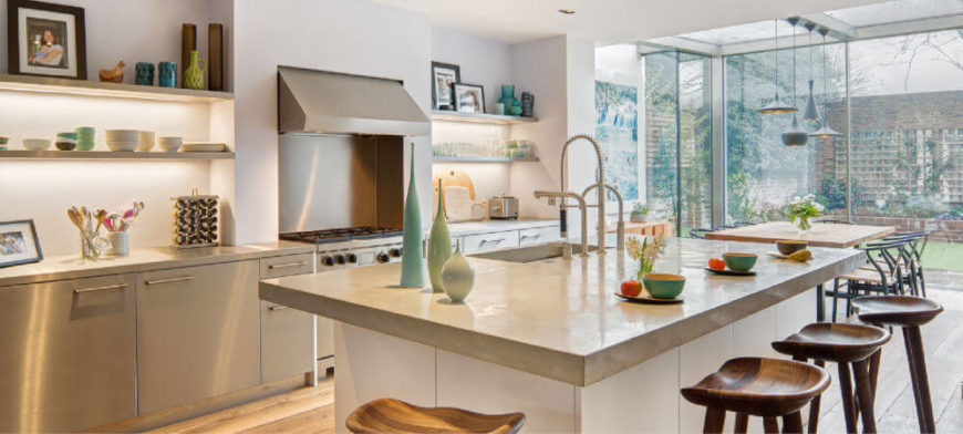 The addition comes directly off of the kitchen, which has been remodeled into a contemporary, sleek, bright kitchen with carved wooden barstools at the eat-in kitchen island. The open shelving to the left of the vent hood and range is backlit. The addition comes directly off of the kitchen, which has been remodeled into a contemporary, sleek, bright kitchen with carved wooden barstools at the eat-in kitchen island. The open shelving to the left of the vent hood and range is backlit.