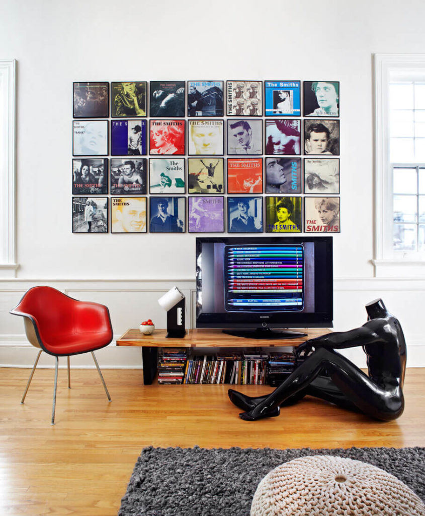 The multi-colored album art prints on this wall, floating above a custom entertainment table and red leather armchair, exemplify the playful yet restrained style of this home. One of several human forms graces the hardwood flooring here. The multi-colored album art prints on this wall, floating above a custom entertainment table and red leather armchair, exemplify the playful yet restrained style of this home. One of several human forms graces the hardwood flooring here.