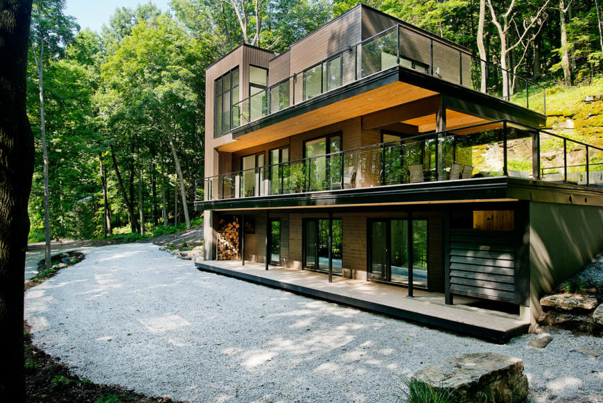 With the full home in view, we see the mixture of wood tones and black metal framing that create the angular, tiered structure. The front is fully exposed while the back recedes into the hillside. With the full home in view, we see the mixture of wood tones and black metal framing that create the angular, tiered structure. The front is fully exposed while the back recedes into the hillside.