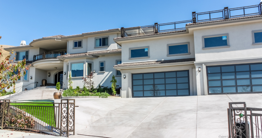 A wrought-iron gate surrounds the sprawling property of this enormous home. The gate leads directly up to either garage. Above the garages we can see a rooftop terrace. A wrought-iron gate surrounds the sprawling property of this enormous home. The gate leads directly up to either garage. Above the garages we can see a rooftop terrace.