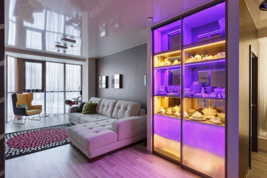 Immediately after the small entrance hallway is the living room, which features a comfy sectional sofa and a lighted display case in orange and purple. Immediately after the small entrance hallway is the living room, which features a comfy sectional sofa and a lighted display case in orange and purple.