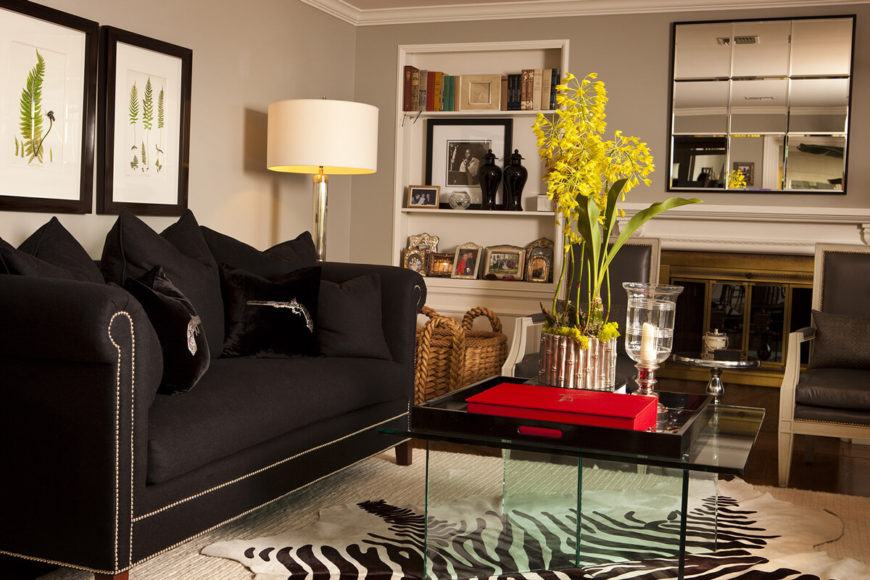 On this end of the room, we see an array of darker hued furniture, centered on an all-glass coffee table. The high contrast space includes lighter toned walls and rich, dark hardwood flooring. On this end of the room, we see an array of darker hued furniture, centered on an all-glass coffee table. The high contrast space includes lighter toned walls and rich, dark hardwood flooring.