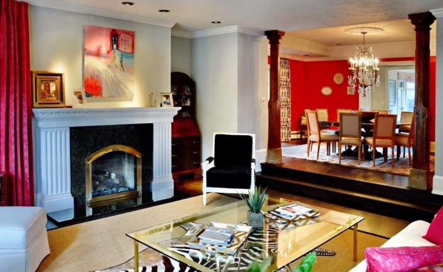 The central living room space is absolutely bursting with color and texture, centered around a black marble fireplace with white mantle. A beige area rug sits atop dark hardwood flooring, with a glass and gold table at center and artwork surrounding. The central living room space is absolutely bursting with color and texture, centered around a black marble fireplace with white mantle. A beige area rug sits atop dark hardwood flooring, with a glass and gold table at center and artwork surrounding.