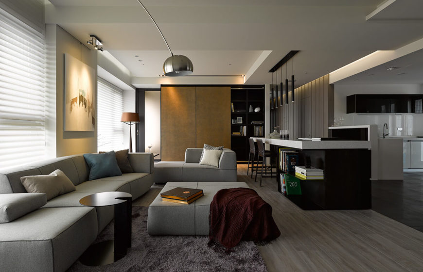 To the right we see the unique island placed outside of the kitchen, defining the edge of this living room space as much as the division between hardwood and tile flooring. There are several ultra-modern touches seen throughout this space, including the slim pendant lighting. To the right we see the unique island placed outside of the kitchen, defining the edge of this living room space as much as the division between hardwood and tile flooring. There are several ultra-modern touches seen throughout this space, including the slim pendant lighting.