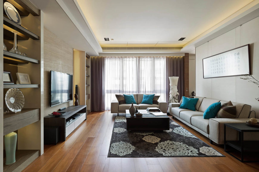 The living room is lit by elegantly subtle recessed lighting in the ceiling edges and built-in shelving. Natural light fills the space as well, via full height windows at the far end. The living room is lit by elegantly subtle recessed lighting in the ceiling edges and built-in shelving. Natural light fills the space as well, via full height windows at the far end.