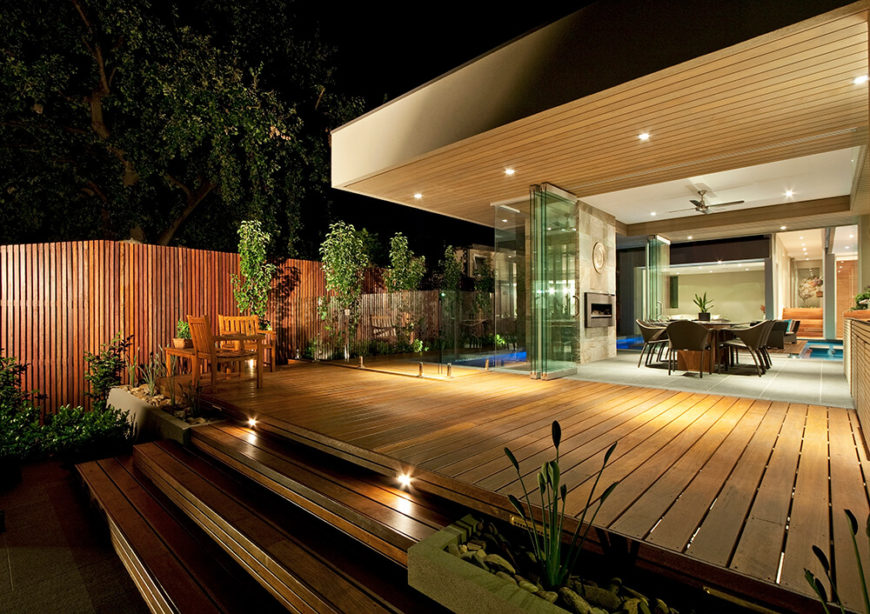 Glancing across the rich hardwood patio at night, we can see deep into the home thanks to both the open-plan design and expanse of retractible glass panels. The intention is to thoroughly blur the line between indoors and out. Glancing across the rich hardwood patio at night, we can see deep into the home thanks to both the open-plan design and expanse of retractible glass panels. The intention is to thoroughly blur the line between indoors and out.