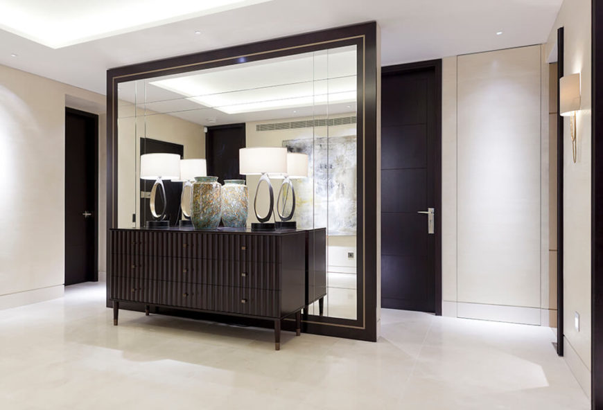 This free standing mirror wall both obscures and expands the visual space in the social area of the home. Framed in a deep black, with decorative elements on a dark dresser in front, it's an essential component of the design. This free standing mirror wall both obscures and expands the visual space in the social area of the home. Framed in a deep black, with decorative elements on a dark dresser in front, it's an essential component of the design.