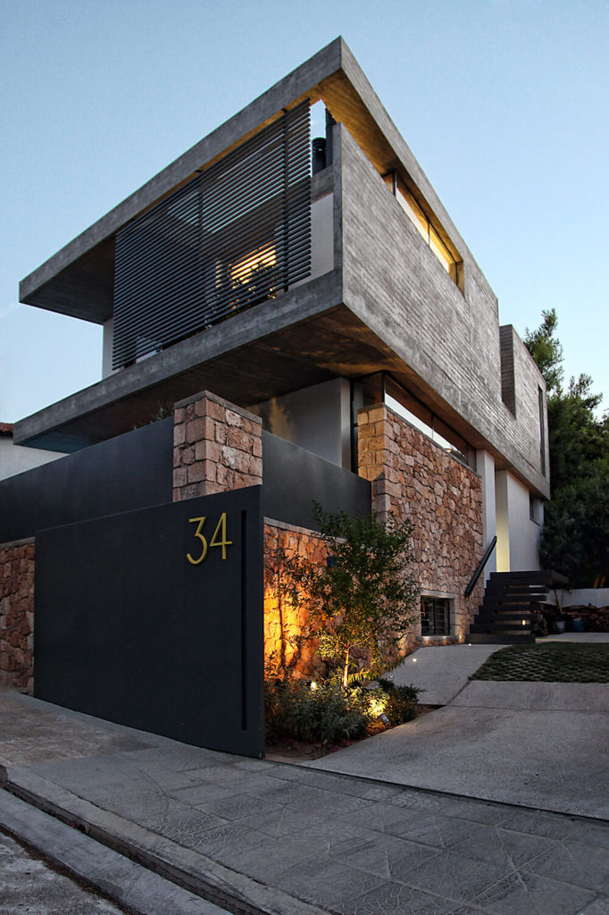 From the exterior, the three levels of this house create a striking visual against the surrounding backdrop. Stone walls crafted of locally sourced stones surround the house, allowing for privacy and creating great contrast against the exposed concrete and black walls used in the rest of the house design. From the exterior, the three levels of this house create a striking visual against the surrounding backdrop. Stone walls crafted of locally sourced stones surround the house, allowing for privacy and creating great contrast against the exposed concrete and black walls used in the rest of the house design.