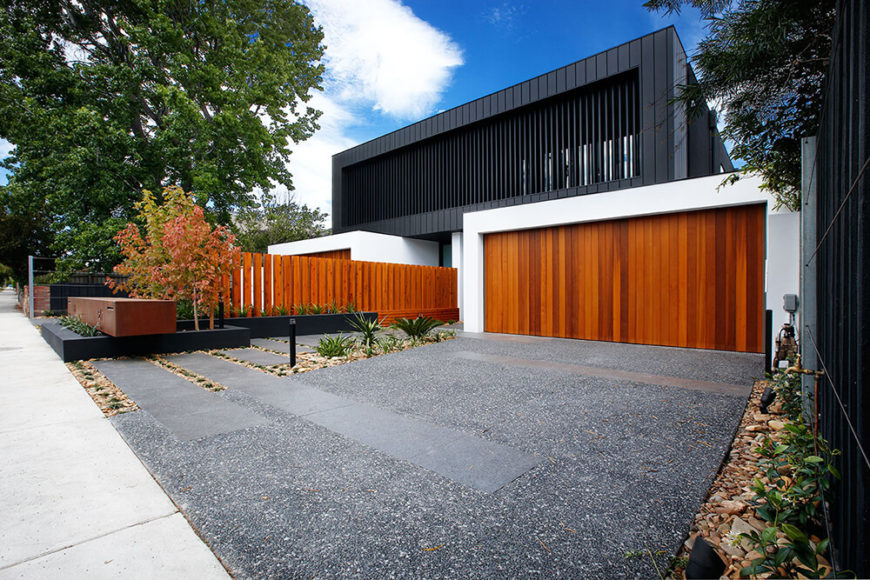 Getting an angled street view of the project, we can see the identical white framed garages, each sporting a rich timber door that matches the dividing fence, supporting the black hued upper section of the structure. Getting an angled street view of the project, we can see the identical white framed garages, each sporting a rich timber door that matches the dividing fence, supporting the black hued upper section of the structure.