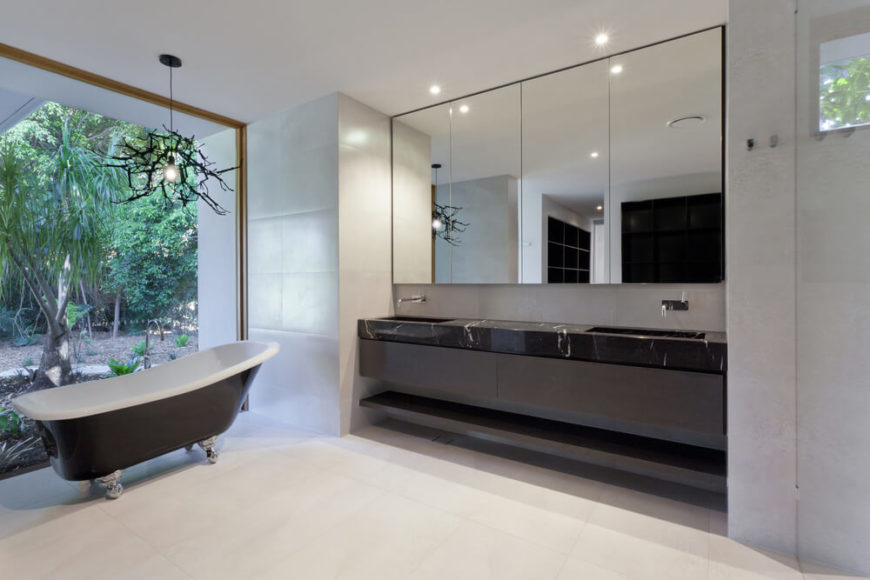 A fine marble counter is home to two sinks, in front of a large mirror in this minimalist bathroom. A clawfoot tub stands to the side, in front of a large window with a view of an outdoor garden. A fine marble counter is home to two sinks, in front of a large mirror in this minimalist bathroom. A clawfoot tub stands to the side, in front of a large window with a view of an outdoor garden.