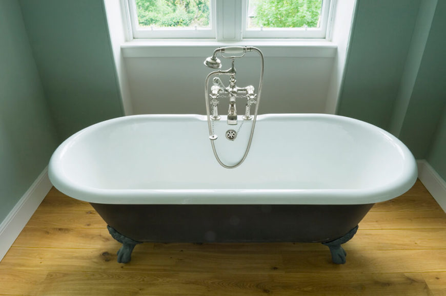 This clawfoot tub is fit for two, and sits upon a lightly stained hardwood floor. The tub is centered beneath a double pane window and is illuminated by the natural light spilling into the room. This clawfoot tub is fit for two, and sits upon a lightly stained hardwood floor. The tub is centered beneath a double pane window and is illuminated by the natural light spilling into the room.