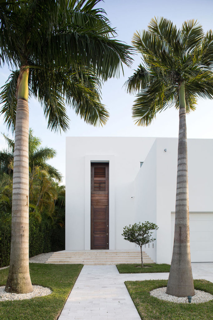 A lovely, if a bit simple row of landscaping leading up to the two-story wooden front door sans mirrors. Enormous palms line the walkway, with a single small fruit tree near the steps leading up to the front door. A lovely, if a bit simple row of landscaping leading up to the two-story wooden front door sans mirrors. Enormous palms line the walkway, with a single small fruit tree near the steps leading up to the front door.