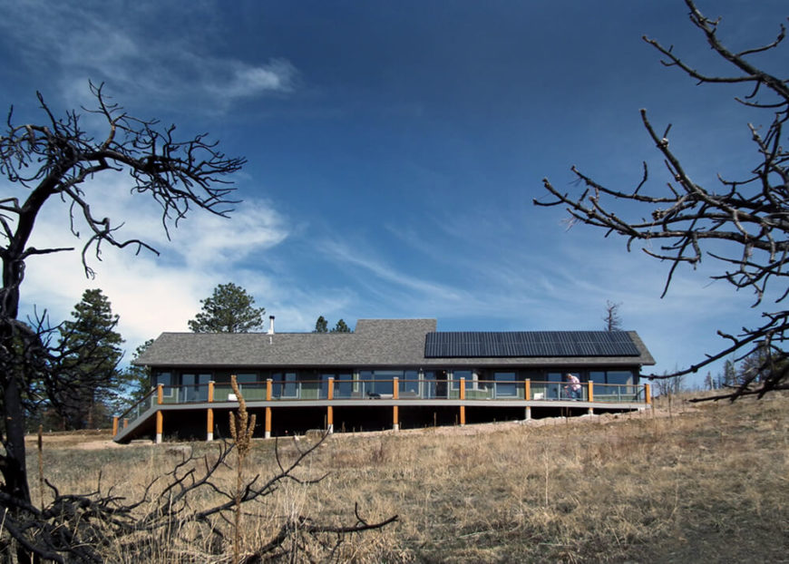 Here we see the broad expanse of the home, with the massive solar array on the roof collecting energy underneath the clear blue sky. The deck can be seen crossing the entire length of the house. Here we see the broad expanse of the home, with the massive solar array on the roof collecting energy underneath the clear blue sky. The deck can be seen crossing the entire length of the house.