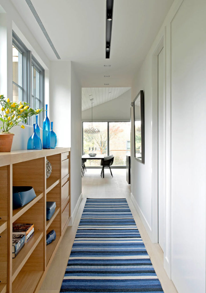 As you enter the Sagaponack Cottage, you'll turn to the right and immediately be greeted by this vibrant blue rug and naturally lit hallway. The white walls help the light bounce around, and the shelving and drawer space to the left provide plenty of area for storage, as well as providing a space for decoration. As you enter the Sagaponack Cottage, you'll turn to the right and immediately be greeted by this vibrant blue rug and naturally lit hallway. The white walls help the light bounce around, and the shelving and drawer space to the left provide plenty of area for storage, as well as providing a space for decoration.