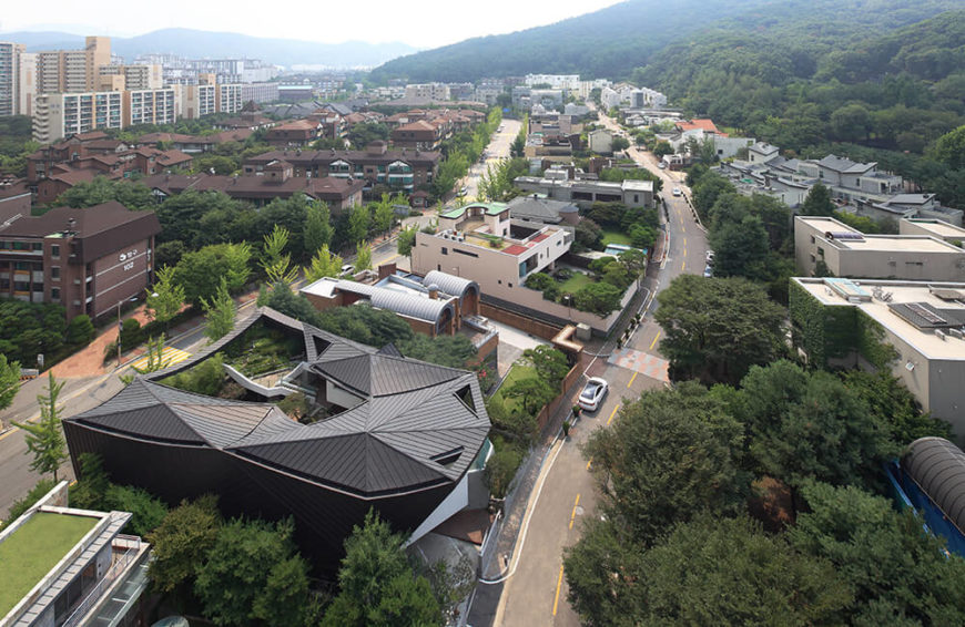 This soaring aerial view of the home and surrounding neighborhood showcases the richly forested environment the home was built in, resting at the foot of vast mountains to the right. This soaring aerial view of the home and surrounding neighborhood showcases the richly forested environment the home was built in, resting at the foot of vast mountains to the right.