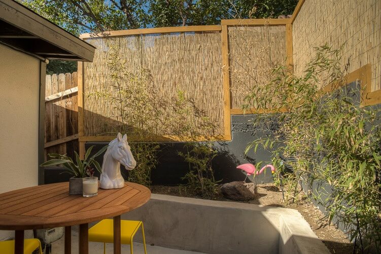 While we can see that as the fencing stretches towards the front of the home, it transitions from reed bamboo on concrete supports to a wooden privacy wall. The planting beds are raised as well, creating a sunken patio area. While we can see that as the fencing stretches towards the front of the home, it transitions from reed bamboo on concrete supports to a wooden privacy wall. The planting beds are raised as well, creating a sunken patio area.
