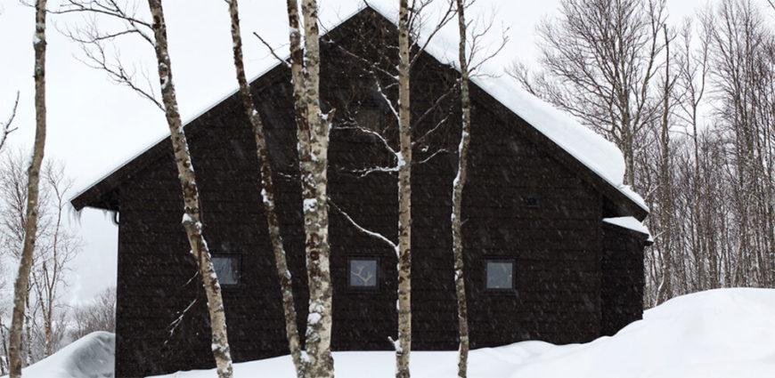 Here we see a set of smaller windows on the side of the home, punctuating the black exterior beneath and above heavy snow. The simple structure belies a sophisticated interior. Here we see a set of smaller windows on the side of the home, punctuating the black exterior beneath and above heavy snow. The simple structure belies a sophisticated interior.