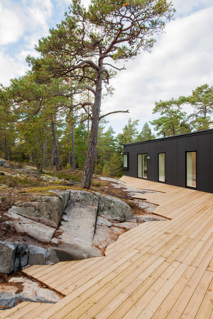 The clean lines of the deck contrast perfectly with the angular, organically cut outer edge, which mirrors the shape of the surrounding rocks. The deck also offers a warm counterpoint to the black of the house facade. The clean lines of the deck contrast perfectly with the angular, organically cut outer edge, which mirrors the shape of the surrounding rocks. The deck also offers a warm counterpoint to the black of the house facade.