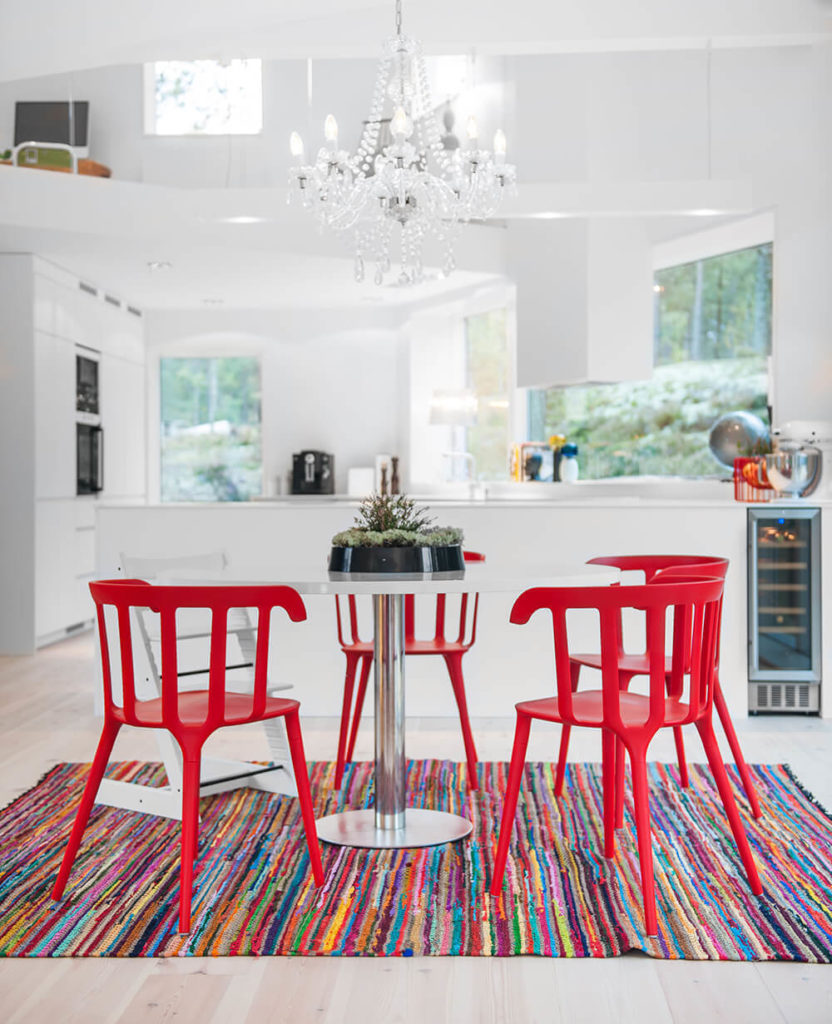 Across the rainbow rug and bright red dining room set, we see the sleekly designed, open plan kitchen below a loft area. This space is illuminated by natural light via sets of large windows all around. Across the rainbow rug and bright red dining room set, we see the sleekly designed, open plan kitchen below a loft area. This space is illuminated by natural light via sets of large windows all around.